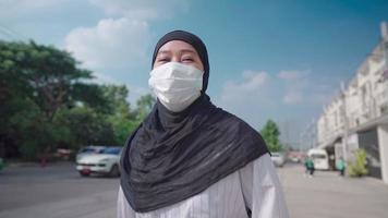 Young asian Muslim female running feeling happy positive, smile under mask rushing along street side outdoor sunny day, new normal Coronavirus COVID-19 pandemic, carefree lifestyle escape from problem video