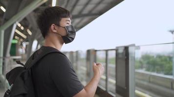 jovem asiático removendo a máscara facial e aliviando a respiração na plataforma do metrô do metrô, impedindo a propagação da pandemia do vírus corona covid-19, novo normal, transporte público, câmera lenta video