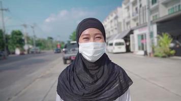ung asiatisk muslimsk kvinna bär skyddande ansiktsmask som går på gatan och känner sig glad positiv, nytt normalt en solig dag, corona covid19 pandemi låsning, risk för infektioner, förhindra virus video