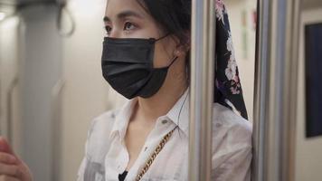 mujer asiática ajusta su máscara protectora negra, parada en el centro del vagón de tren, estación de metro, chica covid dentro de la estación de metro, nuevo estilo de vida normal, autoprotección, cámara lenta