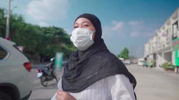 Young south east asian Muslim female running and remove face mask, feeling happy positive, rushing along street side on sunny day, new normal Coronavirus COVID pandemic, freedom life escape from all video