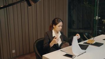 joven mujer de negocios trabajadora con traje de trabajo formal trabaja sola hasta altas horas de la noche en el escritorio de su oficina, lidiando con el contrato de papeleo de la empresa, gestión de análisis de datos, joven emprendedor video