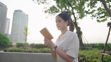 Active young wise asian casual style walking reading book outdoors in sunset at sky park, self study concept, home hobby activity, relaxing walking against modern cityscape view, relaxing city life video