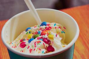 taza con helado de joghurt con toppers dulces como chispas multicolores foto