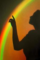 Shadow of woman. Rainbow reflection of sunbeam on wall. Hand touches rainbow beam.