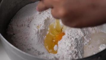 Machen Sie eine Zeitlupenaufnahme, wenn Sie ein Ei in das Mehl schlagen, das für die Zubereitung hausgemachter Desserts vorbereitet ist. video