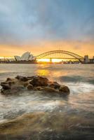 puesta de sol en el teatro de la ópera y el puente del puerto en sydney, estado de nueva gales del sur de australia. foto