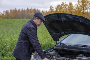 un anciano jubilado abre el capó de su auto y mira el motor foto