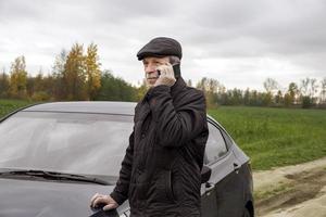 Adult pensioner stands near car and talks on smartphone photo