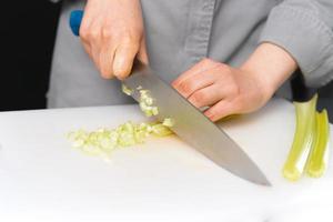 foto de primer plano de una chef cortando apio con un cuchillo en una pizarra blanca