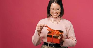 la foto panorámica de una mujer joven sostiene una caja de regalo envuelta en rojo.
