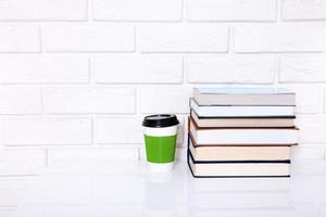 Workplace with cup of coffee and books near brick wall on white table. Copy space and selective focus photo