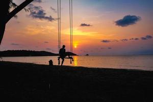 Silhouette People sit on the swing with beautiful sunset cloud sky on the idyllic ocean