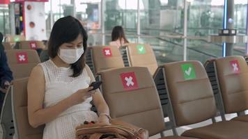 las mujeres asiáticas usan una máscara y se sientan entre sillas para reducir la propagación del coronavirus. los turistas esperan para subirse a los aviones durante el brote de covid-19. video