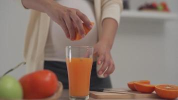 una mujer embarazada está tomando jugo de naranja para agregar vitaminas a su hijo por nacer. las mujeres hacen su propio jugo de naranja comprando la naranja y exprimiendo el jugo. persona saludable. video