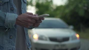 Sicherheit im Notfall. Mann wählt wegen einer Autopanne im Wald ein Handy für eine Notrufnummer. Die Wartung des Autos vor der Fahrt erhöht die Unfallsicherheit. video