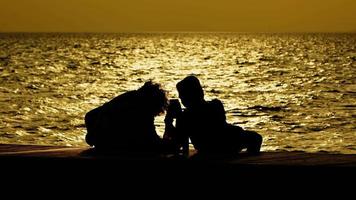 silhueta de pessoas perto do mar ao pôr do sol video