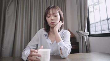 Heart broken Asian woman feel disappointed and unsatisfied, negative feeling lady, sit down alone at home dining desk, holding white coffee mug, contemplation mood, sad blue day, wrong choice making