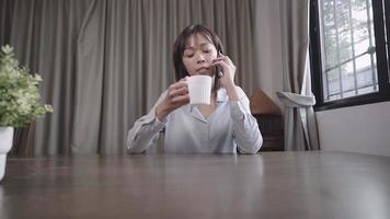 Young short hair female worker talking on cellphone, enjoying sipping on coffee brake while working at home period, drinking and sitting on the chair at home, work from home isolation, epidemic theme video