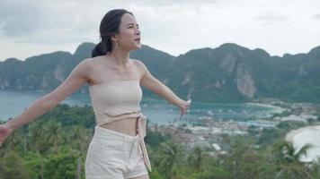 Happy attractive Asian tourist woman enjoys fresh wind on a viewpoint view, looks at mountain forest landscape, young fashionable summer wears, cliff observation activity, natural eco traveling video