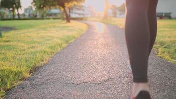 vista posteriore con angolo basso di una giovane donna sportiva che corre all'interno del parco lungo il percorso di corsa, bella luce arancione dell'orizzonte al tramonto, esercizio cardio, inizio di una nuova risoluzione sportiva energia positiva video