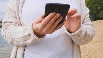vrouw gebruikt moderne smartphone in de natuur. vrouwenhanden gebruiken de telefoon om informatie te zoeken en op internet te communiceren. video