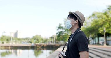 vue latérale d'un jeune homme asiatique avec un masque médical et un chapeau prenant une photo par caméra dans le parc. sécurité et femme heureuse pratiquant la distanciation sociale et la quarantaine. concept de passe-temps et de style de vie. video