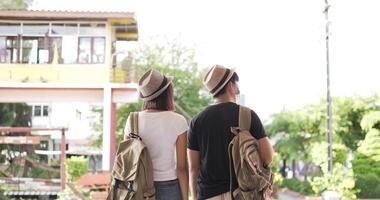 vista posteriore della giovane coppia asiatica del viaggiatore che aspetta il treno alla stazione ferroviaria. uomo e donna che indossano maschere protettive, durante l'emergenza covid-19. concetto di trasporto, viaggio e distanziamento sociale. video