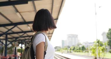 zijaanzicht van jonge Aziatische reizigersvrouw die op de trein wacht bij treinstation. vrouw die beschermende maskers draagt, tijdens covid-19-noodsituatie. transport, reizen en social distancing concept.