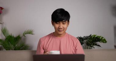 primer plano de un hombre de negocios que trabaja en una computadora portátil y toma café mientras se sienta en un sofá en la sala de estar. autónomo trabajando desde casa. navegar por internet, usar redes sociales. video