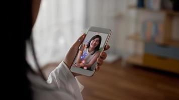 cierre la mano de una mujer asiática usando un teléfono inteligente vertical para ver la transmisión en vivo en las redes sociales mientras sostiene el teléfono móvil divirtiéndose en casa. concepto de tecnología y estilo de vida. video
