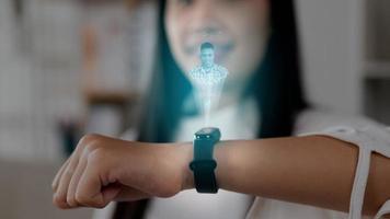 Close up hand of Asian woman pressing buttons on smart watch while sitting on sofa. Projecting visible AR screen and chatting on video call. Futuristic and technological concept.