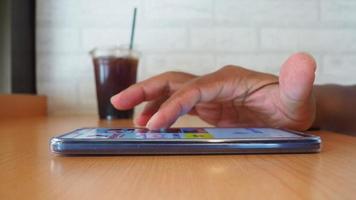 vista laterale della mano dell'uomo che utilizza lo smartphone nella caffetteria per cercare informazioni video