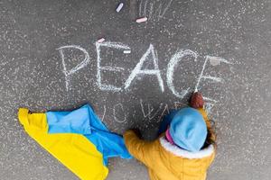 Top view of little girl writing peace with chalk. Protest against Russian invasion of Ukraine. photo