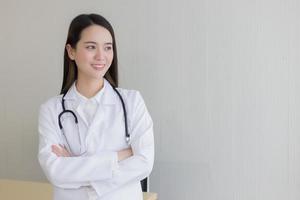 una doctora asiática con el pelo largo y negro lleva una bata de laboratorio blanca y un estetoscopio. foto