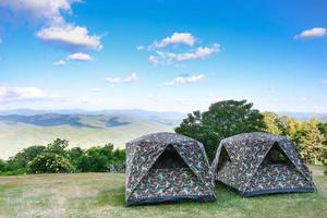 carpa en la colina debajo de las montañas bajo un cielo despejado en un hermoso campamento de verano. la tienda de camuflaje está en campos verdes y montañas al amanecer como papel tapiz de la naturaleza foto