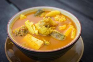 El curry amarillo amargo picante con brotes de coco y pescado de mar es uno de los alimentos del sur de Tailandia en la mesa de madera como fondo. foto