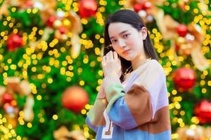 Asian beautiful woman in a colorful sweater stands happily. In his hand he held a light in front of the Christmas tree. With bokeh as background In the theme of Christmas and New Year celebrations photo