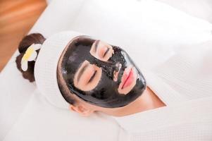 una hermosa mujer asiática usa barro de spa para el tratamiento facial foto
