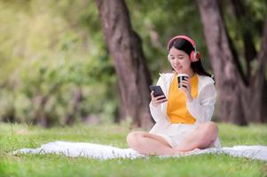 hermosa mujer asiática relajándose en el jardín y usando un teléfono móvil, puede buscar música o comprar en línea en Internet foto