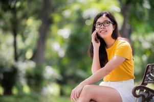 hermosa mujer asiática tendida en el jardín y usando un teléfono móvil, puede buscar información o comprar en línea en Internet foto