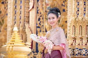 A beautiful elegant Thai woman in Thai dress adorned with precious jewelry stands holding a flower garland photo