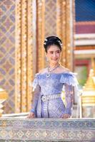 A beautiful, graceful Thai woman in Thai dress adorned with valuable jewelry stands in a beautiful ancient Thai temple photo