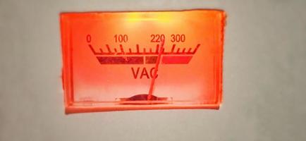 An isolated red-orange old volt ampere meter electrical equipment display under dim condition. photo