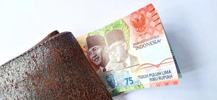 A 75,000 rupiah banknote from Bank Indonesia under the dark orange wallet with a grey background. Issued during the 75 th national independent of Indonesia at 17 August 2020, period of 1945-2020. photo