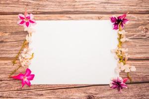 Pink azalea flowers with white asystasia gangetica flowers and blank paper sheet on a wooden background.spring border pink and white blossom, top view, Blank template for your text. flat lay. photo