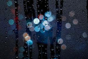 gotas de lluvia en la ventana y luces de la calle por la noche foto