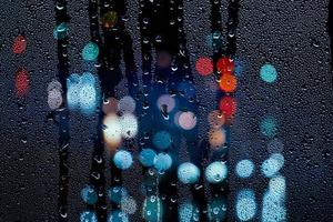 gotas de lluvia en la ventana y luces de la calle en la noche foto