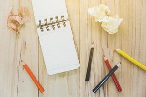 Small note book paper or notepad for writing information with color pencil and crumpled paper balls on wooden table. view from above photo