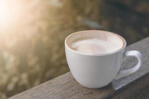 taza de capuchino de café caliente con espuma de leche en el balcón de madera foto
